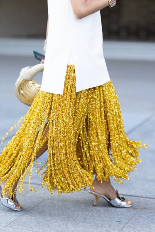 Guest wears a white top, a yellow long skirt made of paillettes fringes, silver and gold heeled sandals and a white and light yellow Bottega Veneta...