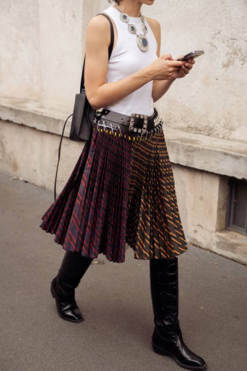 Guest wears a white top, pleated skirt, and long boots outside Prada during the Milan Fashion Week - Womenswear Spring/Summer 2024 on September 21,...