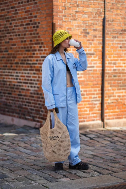 Guest wears a yellow fishnet / mesh bob hat from Prada, a black shoulder-off / cropped top, a pale blue cotton shirt from Prada, matching pale blue...