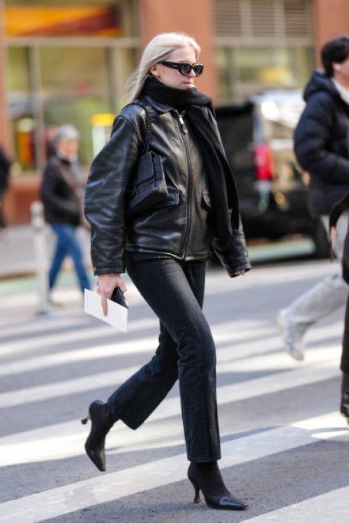 Guest wears Alaia sunglasses, a black scarf, a black leather jacket, black denim pants / jeans , pointed boots, outside Calvin Klein, during New York...