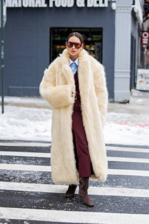 Guest wears beige fur coat, burgundy skirt, blouse, suede outside Ulla Johnson during New York Fashion Week on February 09, 2025 in New York City.