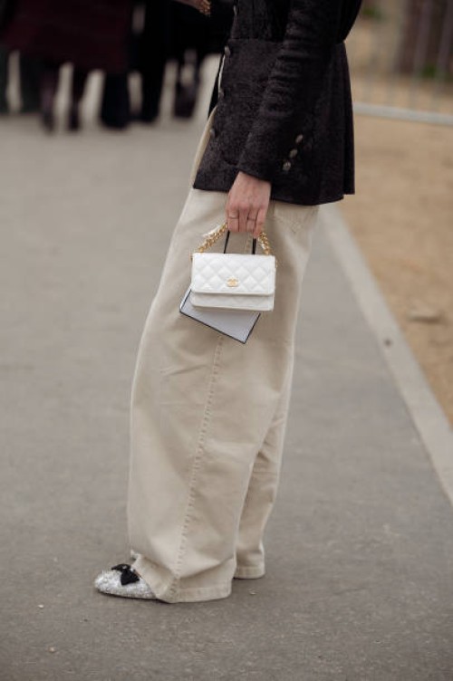 Guest wears beige pants, blakc jacket and white bag outside Chanel during the Womenswear Fall/Winter 2024/2025 as part of Paris Fashion Week on March...