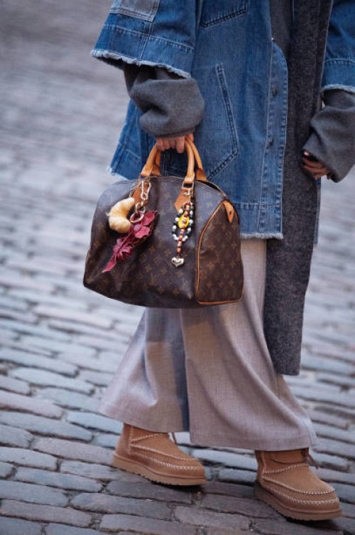 Guest wears beige skirt, brown shoes, denim jacket, grey long scarf and brown Louis Vuitton bag with accessories outside the Gestuz fashion show...