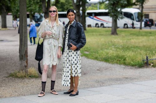 Guest wears belted dress, black net bag & a guest wears black leather jacket, white dress with graphic print outside Horror Vacui during the Berlin...