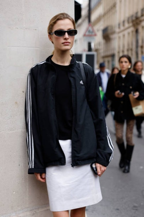 Guest wears black Adidas jacket, white mini skirt, outside The Row, during Womenswear Spring/Summer 2025 as part of Paris Fashion Week on September...