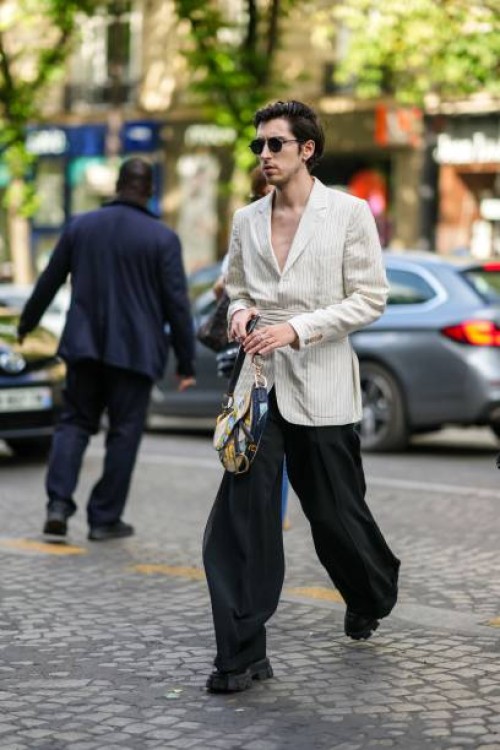 Guest wears black circle sunglasses, a white latte striped print pattern belted blazer jacket, rings, a beige and navy blue painted pattern leather...