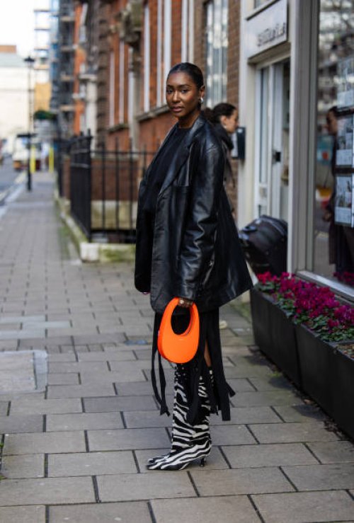 Guest wears black leather jacket, zebra print boots, orange Coperni bag outside Bora Aksu during London Fashion Week February 2024 on February 16,...