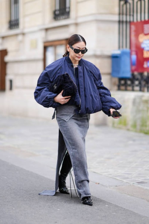 Guest wears black Saint Laurent / YSL sunglasses, a blue bomber jacket, black navy blue quilted velvet Chanel bag, a grey denim slit skirt, outside...