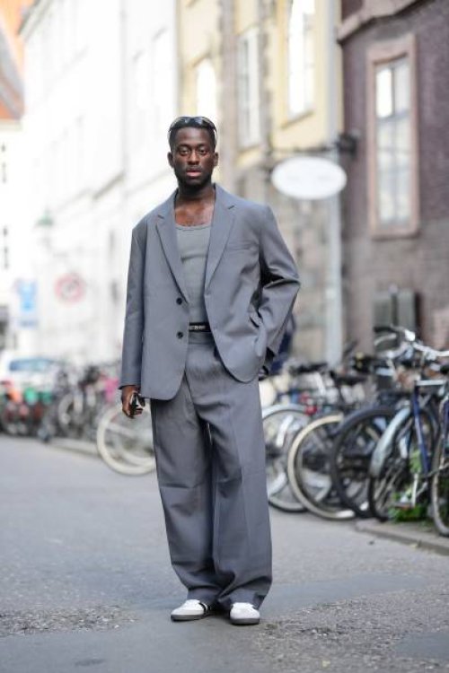 Guest wears black sport sunglasses, a gray tank-top, a gray oversized blazer jacket, matching gray large suit pants, white leather and gray suede...
