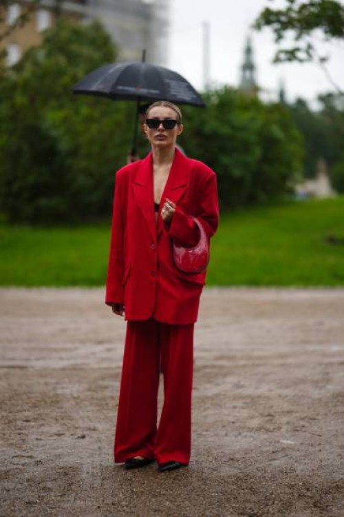 Guest wears black sunglasses, a black bra underwear, a neon red blazer jacket, neon red wide legs pants, a red shiny varnished leather handbag, black...