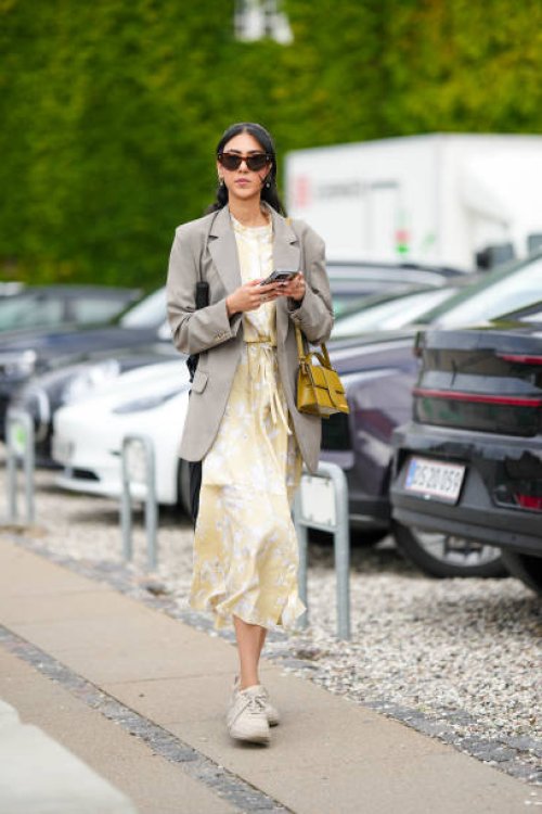 Guest wears black sunglasses, a pale gay long blazer jacket, a pale yellow with white embossed pattern long dress, a yellow shiny leather long...