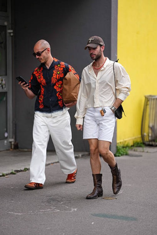 Guest wears black sunglasses, black bright cherry red floral pattern/print buttoned up short sleeve shirt, dark brown leather toe bag, white baggy...