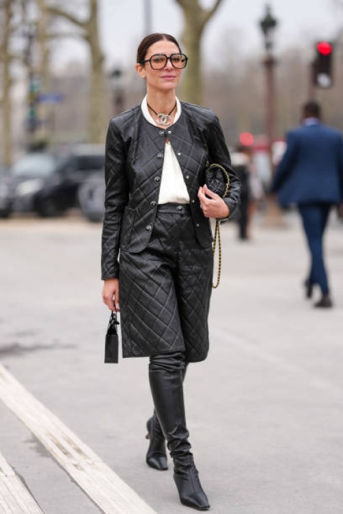 Guest wears black sunglasses, black silver Chanel choker necklace, white shirt, shiny black quilted Chanel leather jacket, gold bracelets, a gold...
