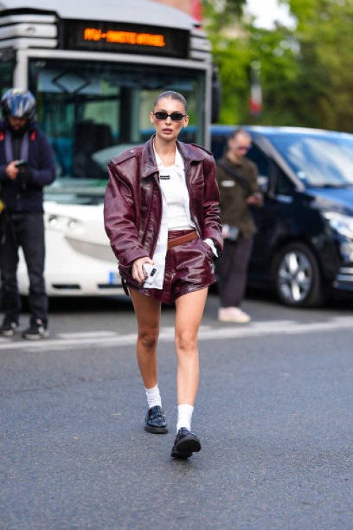 Guest wears black sunglasses, cream tank top, white unbuttoned long sleeve shirt, shiny dark red oversized biker leather jacket, dark brown leather...