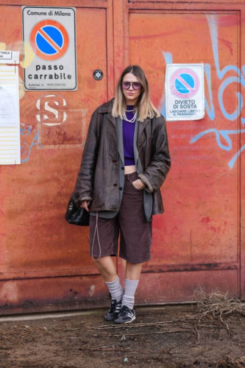 Guest wears black sunglasses, dark purple sweater, white layered pearl necklaces, dark gray oversized blazer jacket, shiny dark brown leather jacket,...