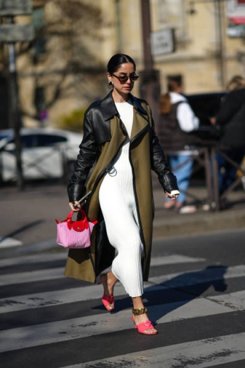 Guest wears black sunglasses, gold and rhinestones earrings, a white ribbed long dress, a khaki fabric and black leather shoulder long coat, a pink...
