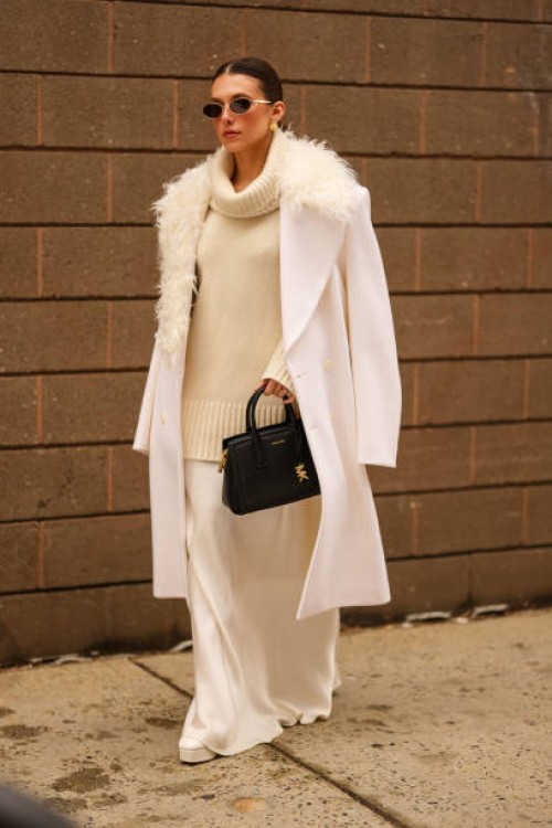 Guest wears black sunglasses, gold earrings, cream knit high neck oversized sweater, white oversized double breasted Michael Kors blazer coat with...