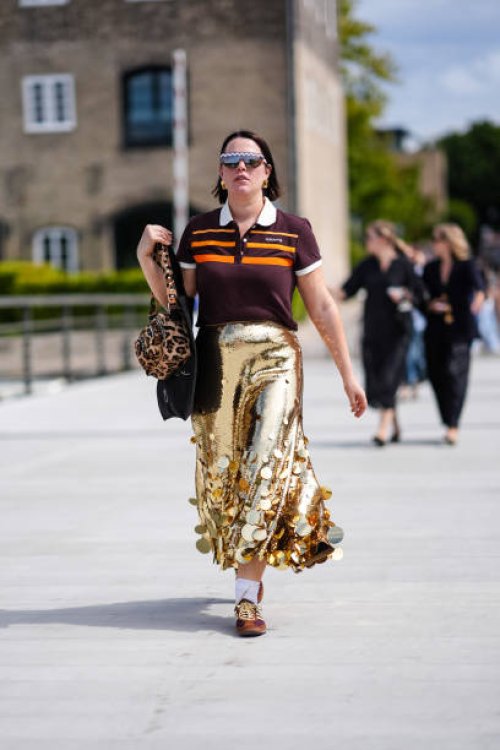Guest wears black sunglasses, gold earrings, dark red brown bright orange striped Adidas Originals 80S short sleeve shirt, light brown and dark brown...