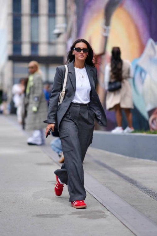 Guest wears black sunglasses, gold earrings, gold layered necklaces, white tank top, dark gray blazer jacket, cream bag, dark gray pants, bright red...
