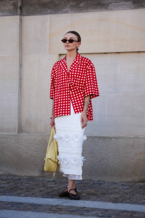 Guest wears black sunglasses, gold earrings, white and red pattern button up short sleeve shirt, silver bracelet, light yellow leather bag, white...