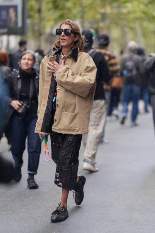 Guest wears black sunglasses, light brown / cream jacket, a black lace skirt with floral details, black sneakers shoes, outside Hermes, during...