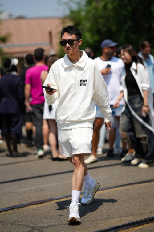 Guest wears black sunglasses, necklaces, a white latte with embroidered black logo pattern long sleeves / polo neck sweater from Miu Miu, white sport...