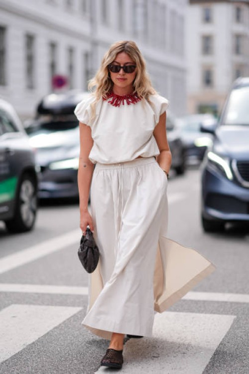 Guest wears black sunglasses, red necklace, white puffy short sleeve shirt, white maxi skirt with slit, black leather Bottega Veneta bag, black sheer...