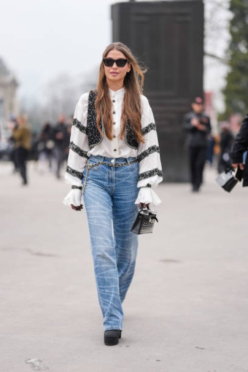 Guest wears black sunglasses, silver earrings, white buttoned up long sleeve black lace striped pattern shirt, black sequin embroidered vest, silver...