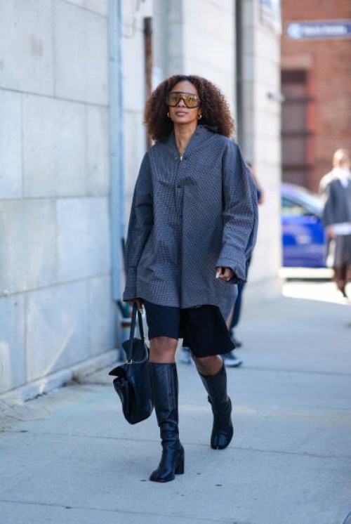 Guest wears black sunglasses, silver earrings, dark gray oversized long sleeve shirt, silver rings, shiny black leather bag, black shorts, shiny...