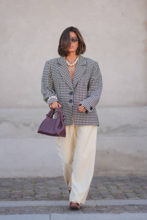 Guest wears black sunglasses, silver necklace, white beaded necklace, black and white pattern oversized blazer jacket, silver rings, white pearl...
