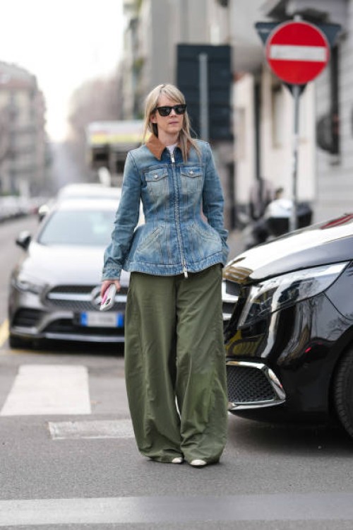 Guest wears black sunglasses, white t-shirt, light blue washed denim jean tailored zipped Alexander McQueen jacket, olive green loose trouser pants,...