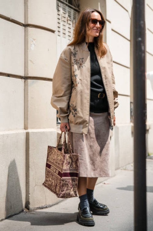 Guest wears black t-shirt, beige printed jacket, beige midi skirt, Dior burgundy tote bag, black loafers, outside Dior Homme, during the Haute...