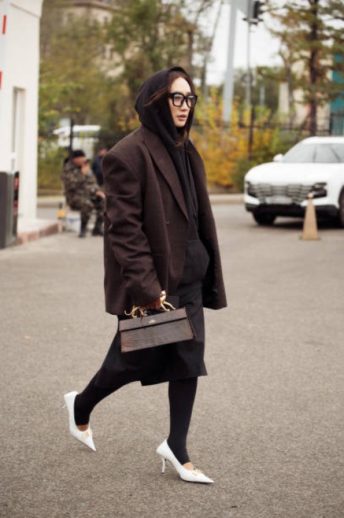 Guest wears black tights, white pointy shoes, brown bag with golden details, black hoodie and brown oversized blazer and black skirt during the 10th...