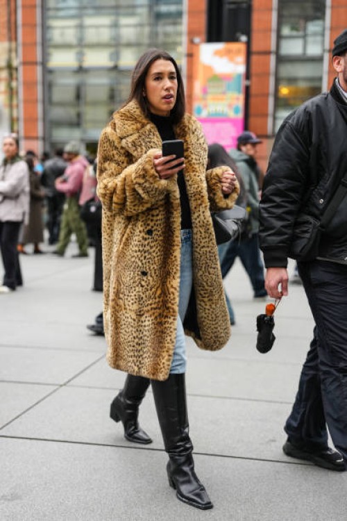 Guest wears black turtleneck long sleeve shirt, light blue denim jean pants, light brown cheetah animal pattern/print faux fur coat, shiny black...
