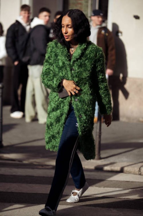 Guest wears blue Adidas pants, a green fur coat, and white ballet shoes with crystal decorations outside Ferrari during the Milan Fashion Week -...