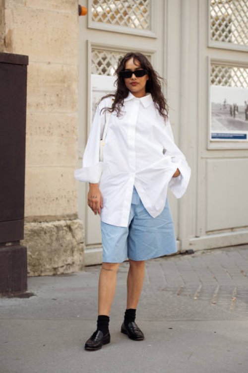 Guest wears blue bermuda shorts, a white shirt, black socks, black shoes, and sunglasses outside Patou during the Haute Couture Fall/Winter 2024/2025...