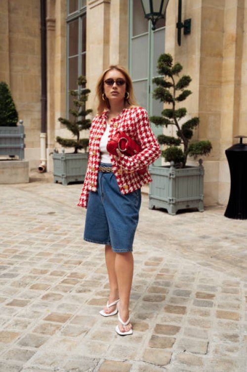 Guest wears blue denim Bermuda shorts, a white top, a red and white checkered jacket, and a red Gucci bag outside Peet Dullaert during the Haute...