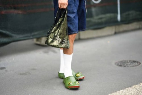 Guest wears blue denim shorts, a green sequined handbag, white socks, green plastic with yellow eyes and red lips mules in shape of frog , outside JW...