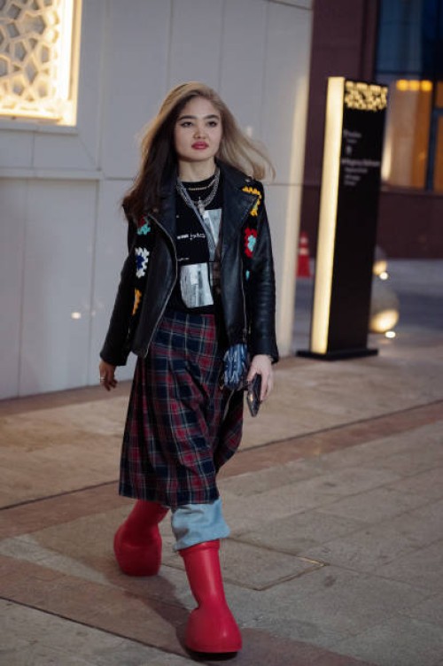 Guest wears blue jeans, a red and black checkered skirt, red boots, and a black leather jacket with knitted colorful elements during the Tashkent...
