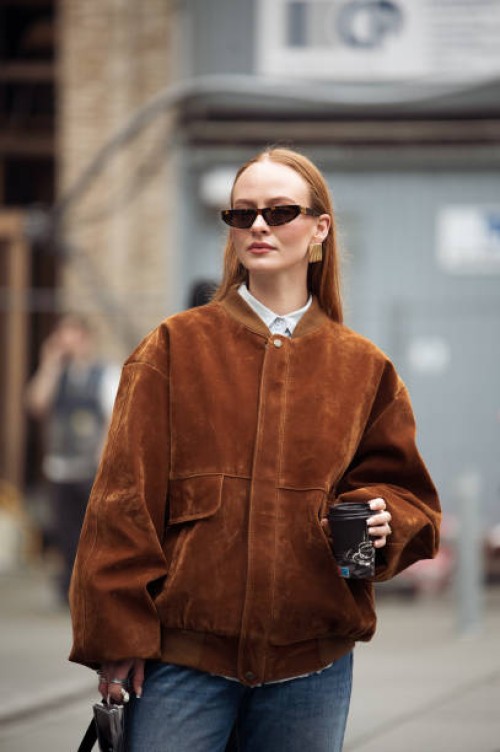 Guest wears blue jeans, brown suede jacket and black bag outside the Herskind fashion show during the Copenhagen Fashion Week Autumn/Winter 2025 on...