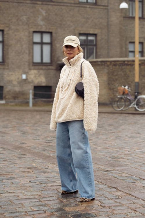 Guest wears blue jeans, fur jumper, pearl necklace, beige cap, and Loewe black bag outside Rolf Ekroth during the Copenhagen Fashion Week AW24 on...