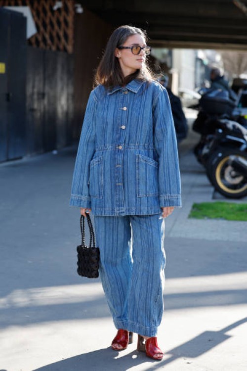 Guest wears blue striped denim jacket with matching jeans, red heels, black bag, outside Stella McCartney, during the Womenswear Fall/Winter...