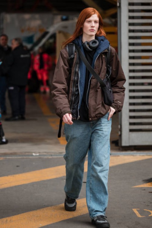 Guest wears blue sweatshirt, brown jacket, jeans, black crossbody bag, outside Ferragamo, during the Milan Fashion Week - Womenswear Fall/Winter...
