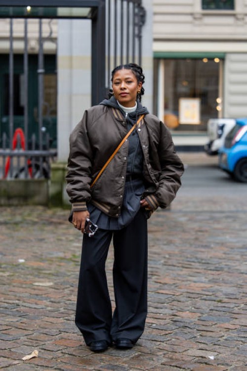 Guest wears brown bomber jacket, grey skirt, pants, black Louis Vuitton bag outside TG Botanical during the Copenhagen Fashion Week Autumn/Winter...