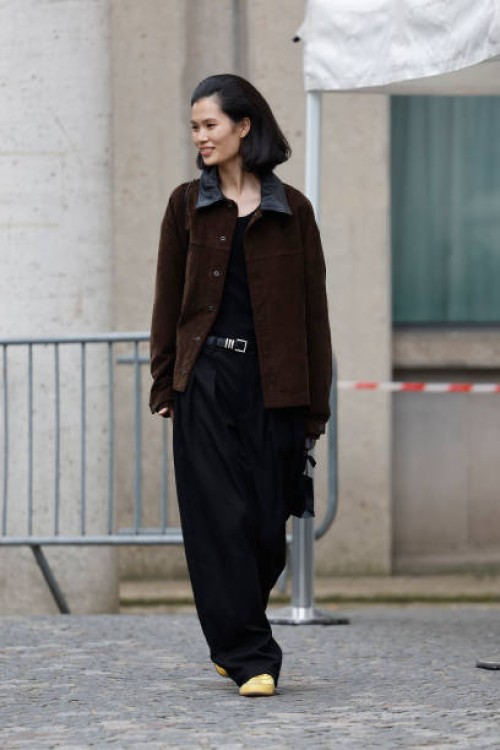 Guest wears brown jacket with leather collar, black trousers, yellow sneakers, outside Miu Miu, during the Womenswear Fall/Winter 2025/2026 as part...
