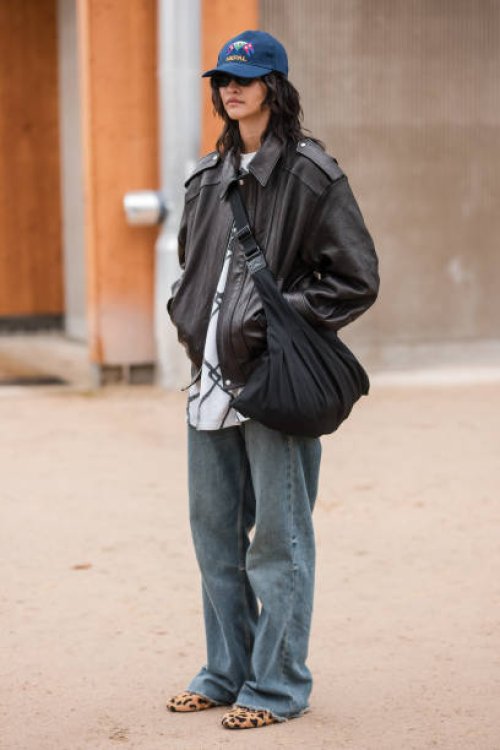 Guest wears brown leather jacket, baggy jeans, blue hat, leopard print flat shoes, outside Chanel, during the Haute Couture Spring/Summer 2024 as...