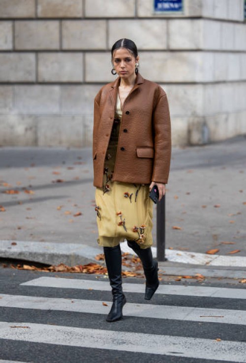 Guest wears brown leather jacket, beige embroidered dress, black boots outside Miu Miu during the Womenswear Spring/Summer 2024 as part of Paris...