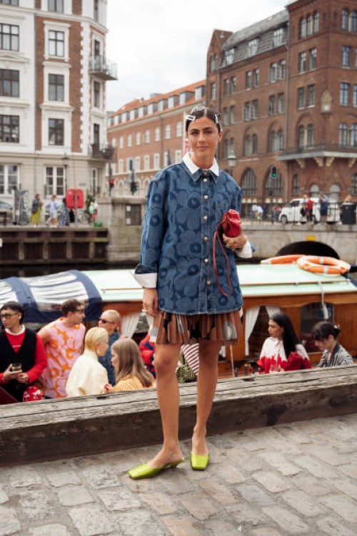 Guest wears brown mini skirt, blue denim shirt, red bag and green flats VIP guest trip with a boat to the Marimekko show during day four of the...