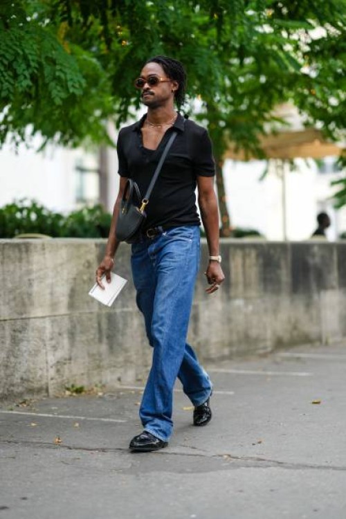 Guest wears brown sunglasses from Celine, a gold necklace, a black short sleeves t-shirt, a black matte leather crossbody bag, blue denim large...