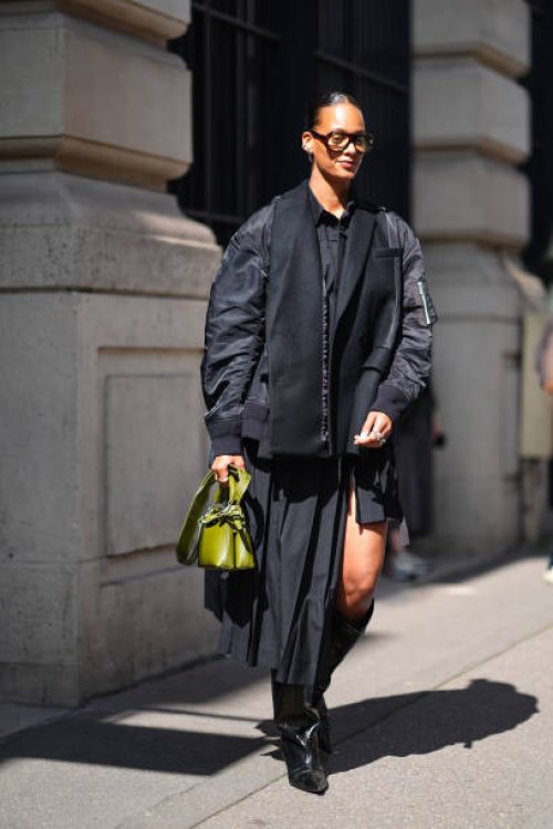 Guest wears brown sunglasses, silver earrings, black button up long sleeve shirt, black shiny black blazer bomber jacket, a light green leather bag...